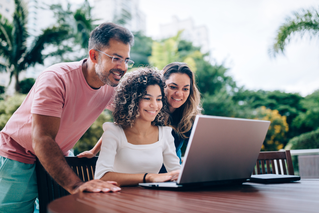 parents gathered around young girl all looking at a laptop, smiling