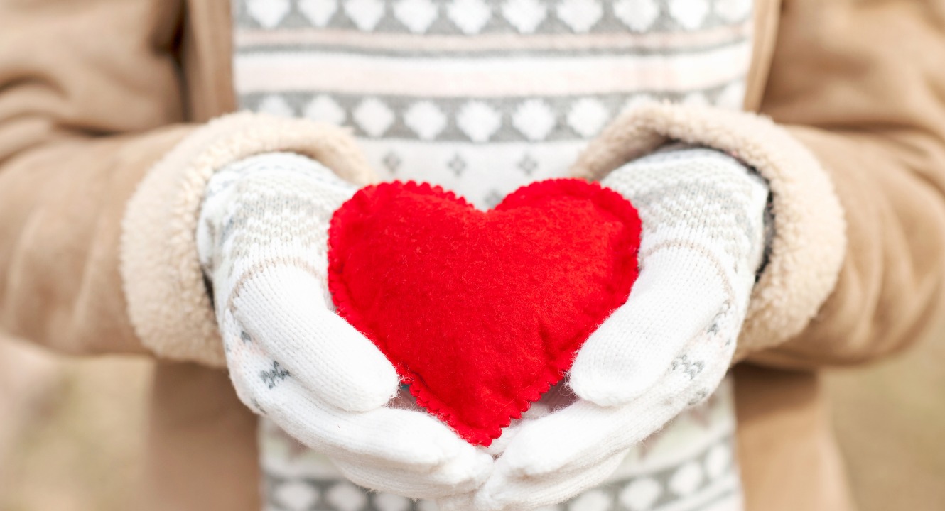 girl wearing mittens holding a bright red heart in her hands