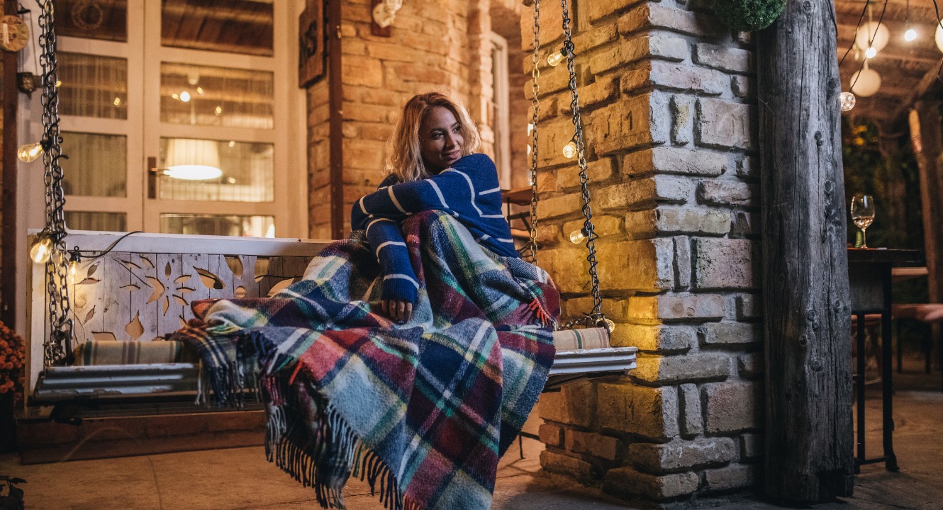 woman snuggled up with a blanket on a front porch swing